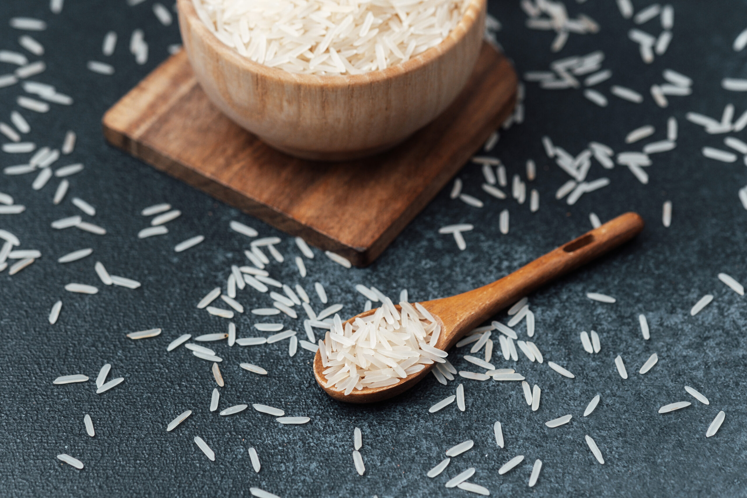 White rice in wooden bowl with scattered grains and wooden spoon