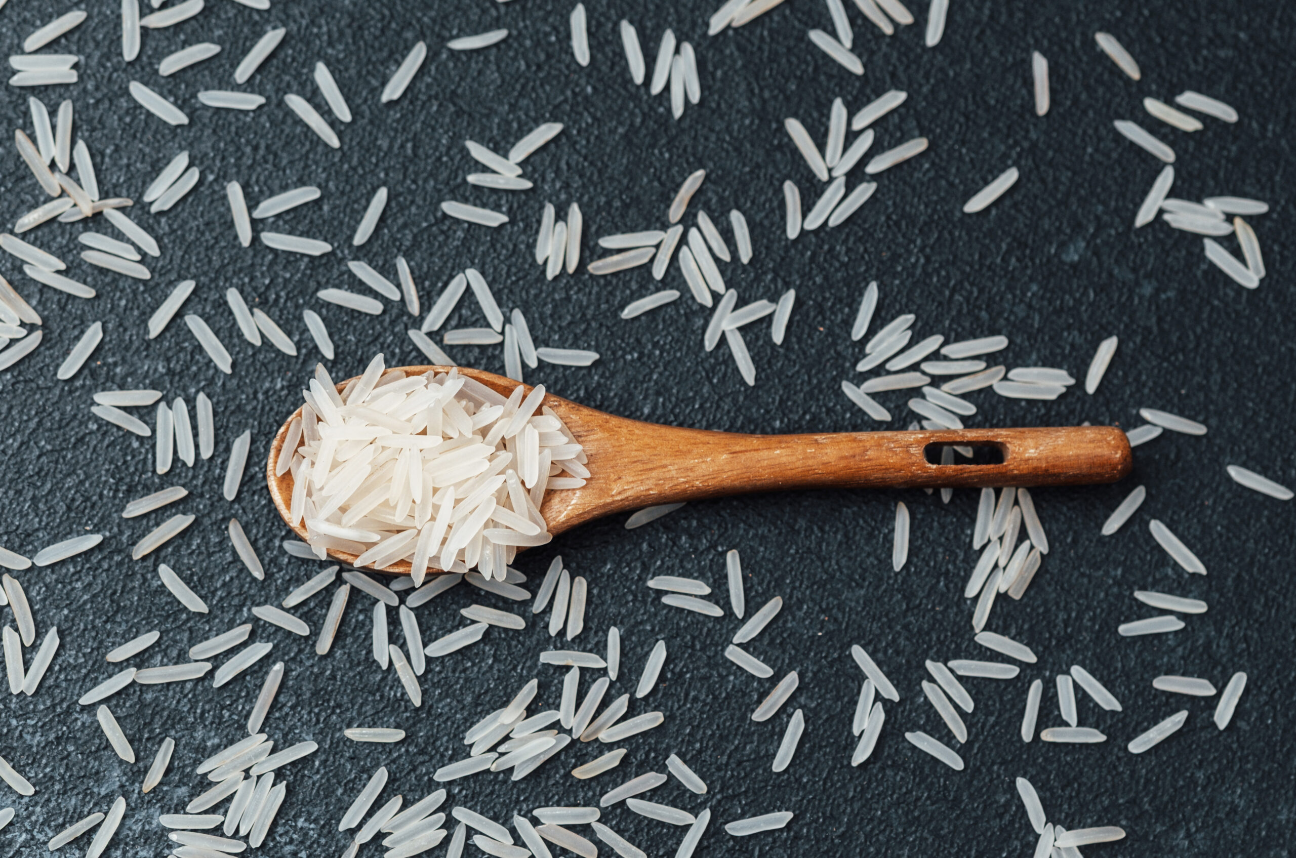 Wooden spoon with white rice grains on dark textured background